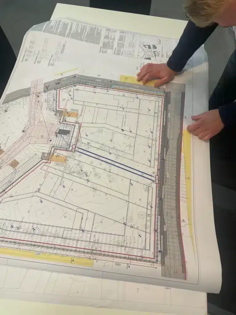 Eine Person betrachtet auf einem Tisch große Architekturentwürfe und studiert dabei detaillierte Baupläne und technische Zeichnungen.