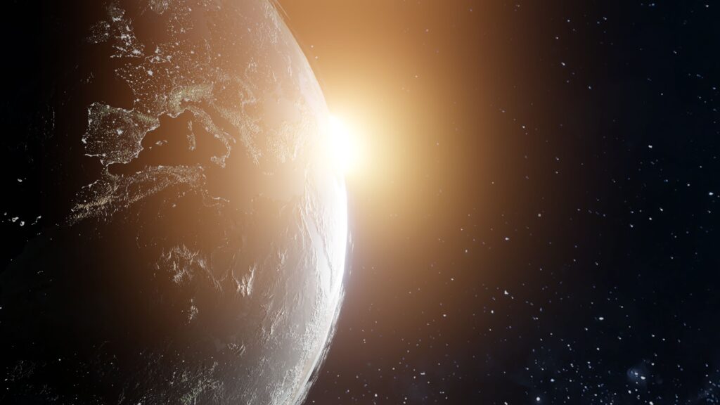Die Sonne geht im Weltraum über dem Horizont der Erde auf und beleuchtet einen Teil des Planeten, während auf der dunklen Seite die Lichter der Städte zu sehen sind. Im Hintergrund ist ein sternenreicher Himmel zu sehen.