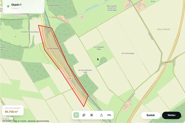 Eine digitale Karte zeigt einen hervorgehobenen, umrandeten Bereich in der Nähe der Straße K25, umgeben von Feldern und beschrifteten Wegen, mit Trassify-Navigationsschaltflächen unten rechts.